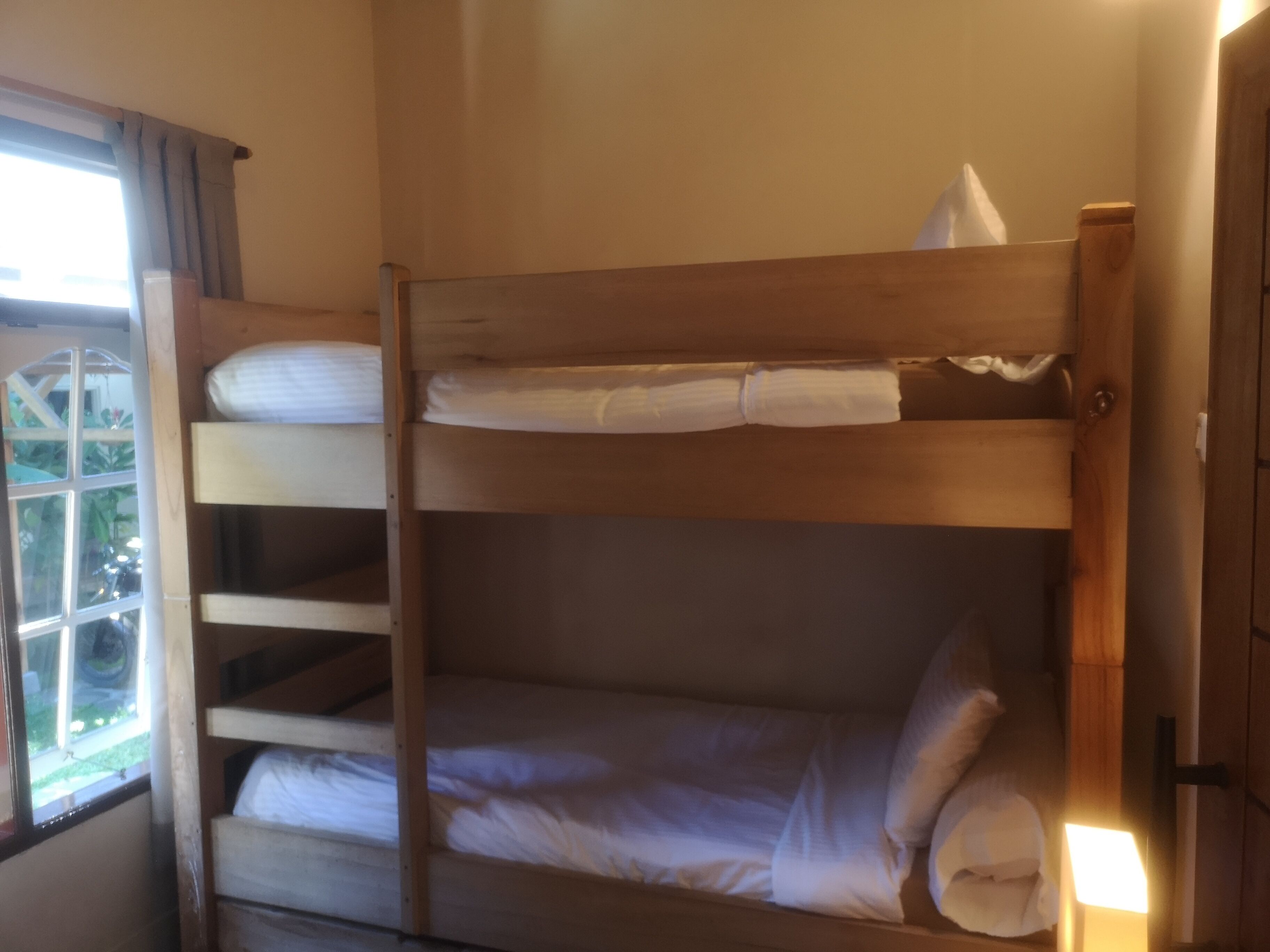 A bunk bed with white bedding and a window with curtains.