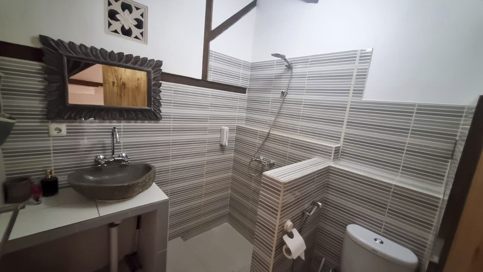A bathroom with a large mirror, a sink, a shower, and a toilet.