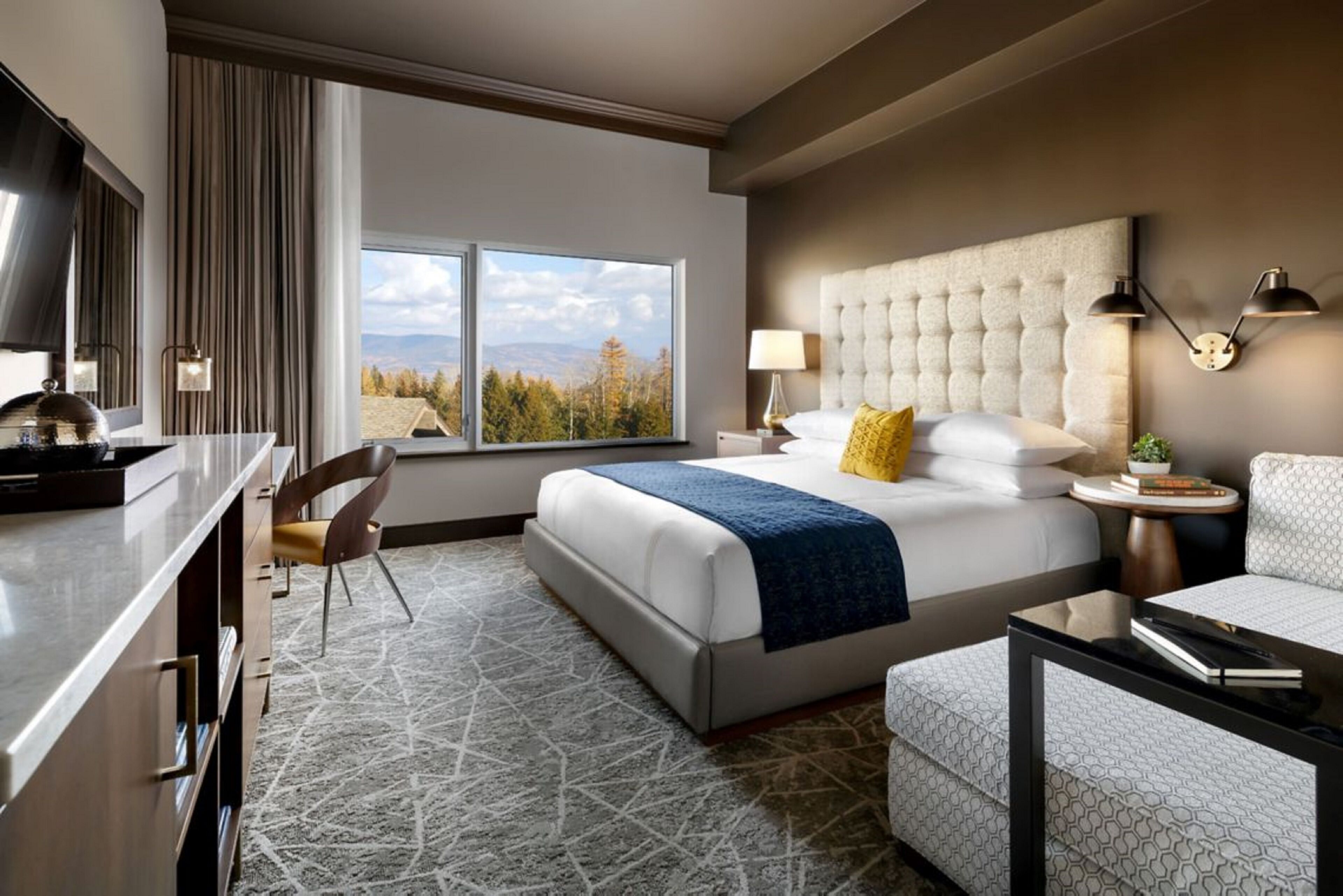 Une chambre d’hôtel avec un grand lit, un bureau, une chaise, un canapé et une vue sur les montagnes.