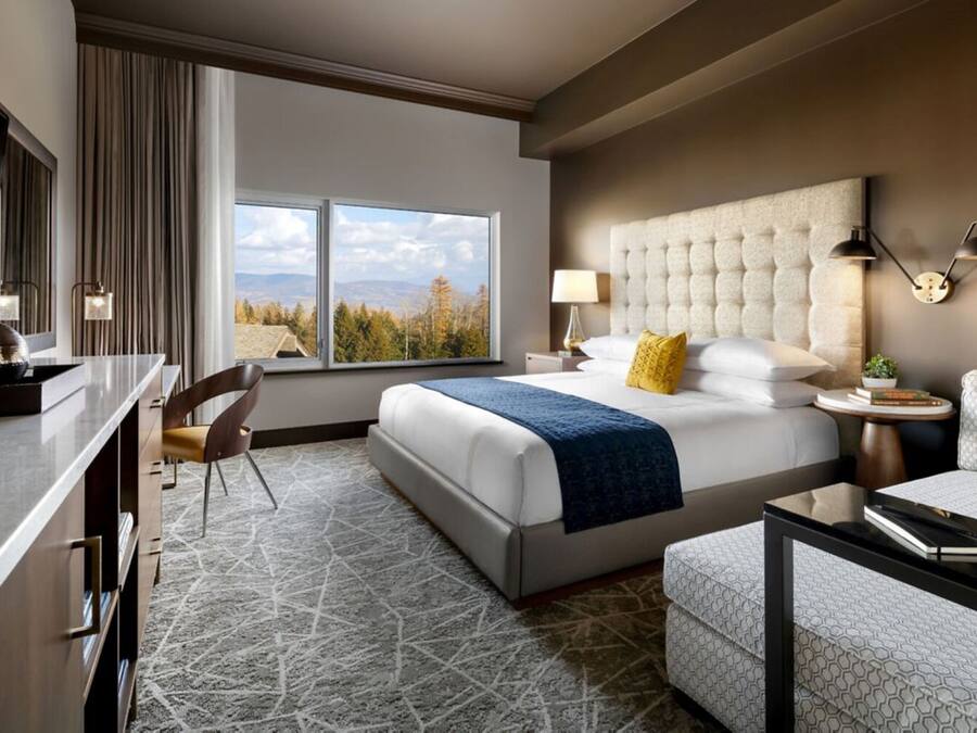 Une chambre d’hôtel avec un grand lit, un bureau, une chaise, un canapé et une vue sur les montagnes.