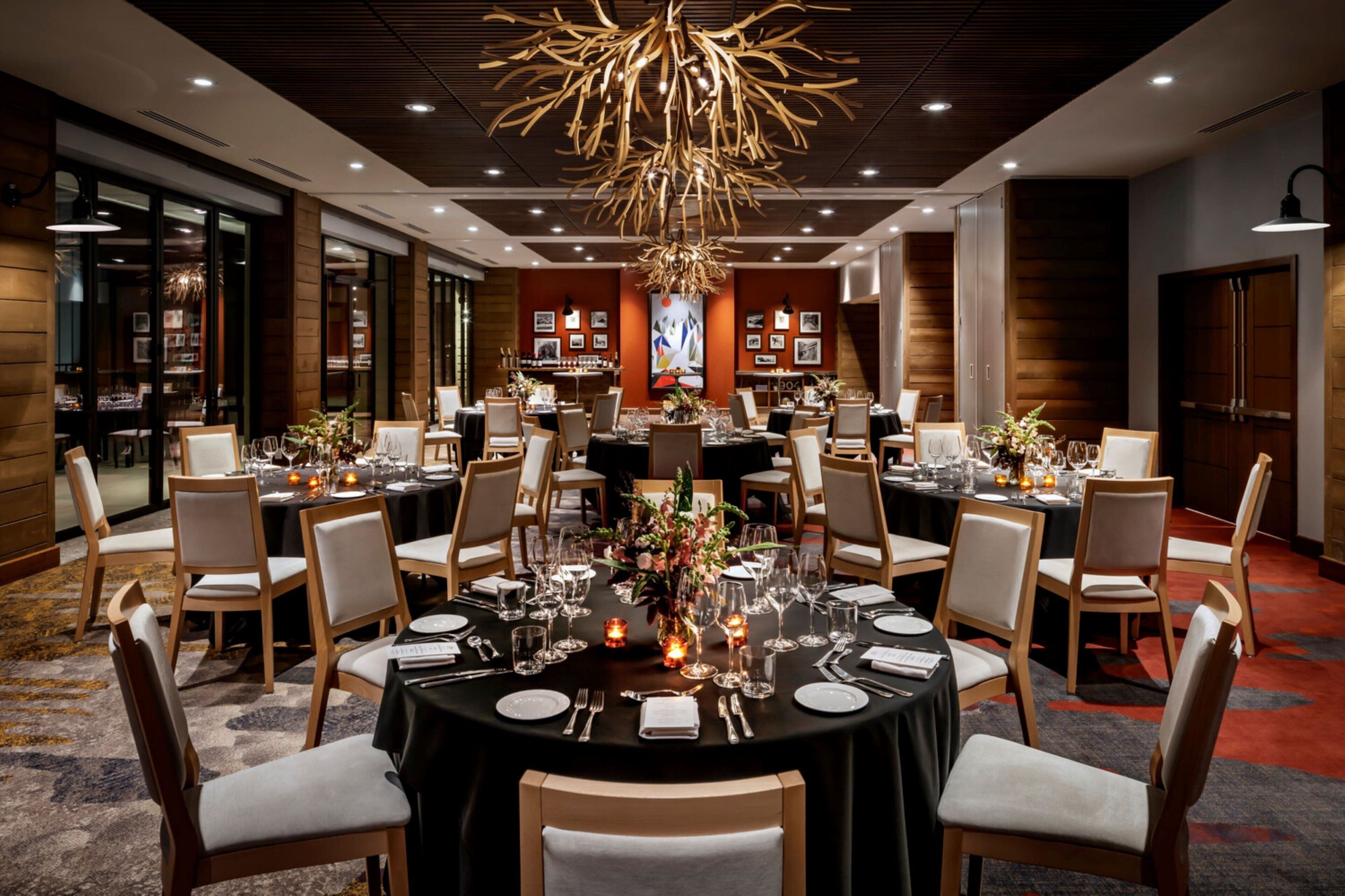Un comedor formal con mesas redondas, sillas y una lámpara central de candelabro.