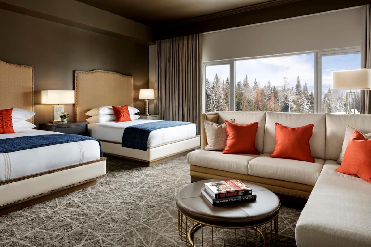 A hotel room with two beds, a sofa, a coffee table, and a large window with a view of trees.