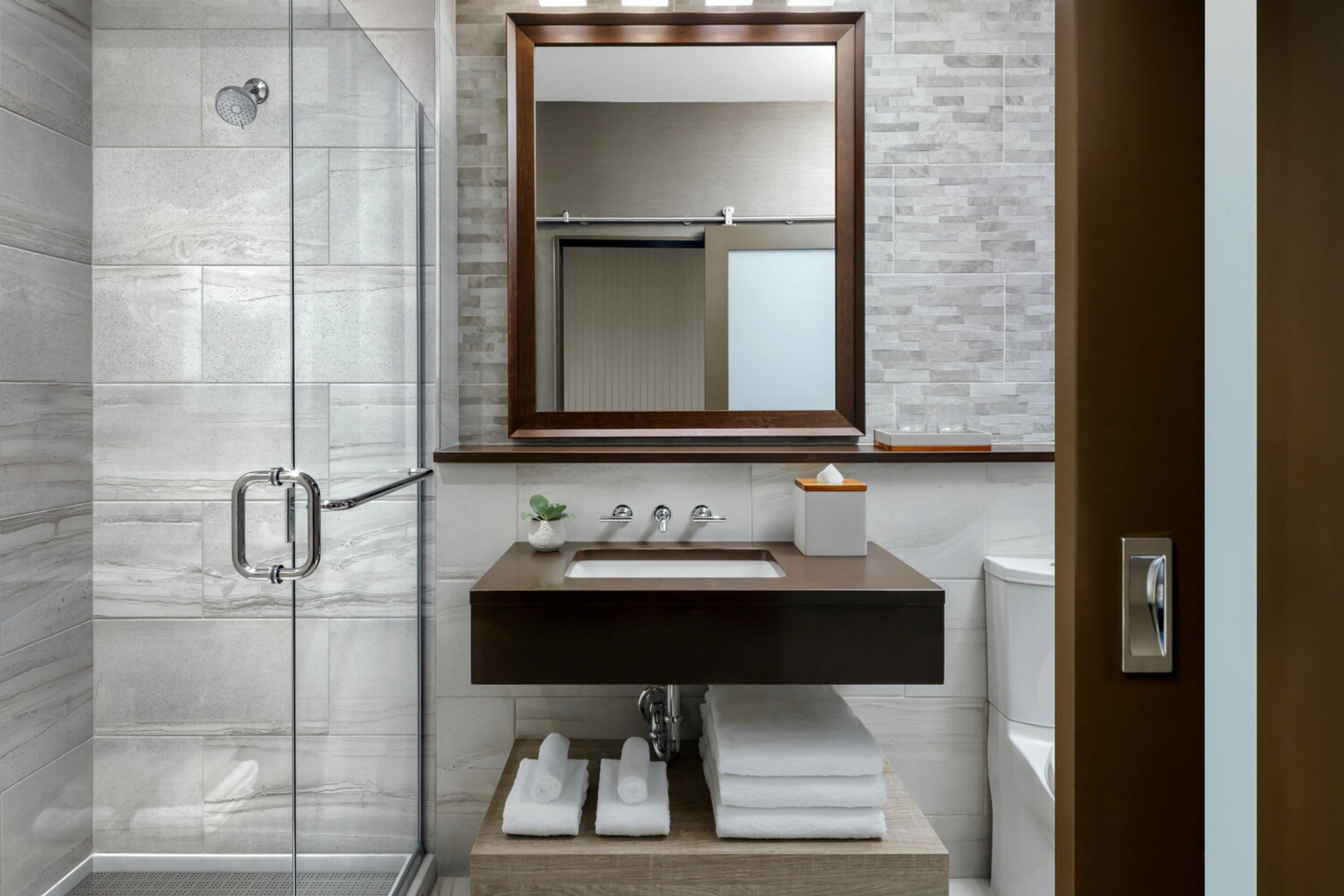 Un bagno moderno con box doccia in vetro, un mobile bagno in legno con lavello e specchio sopra il lavello.