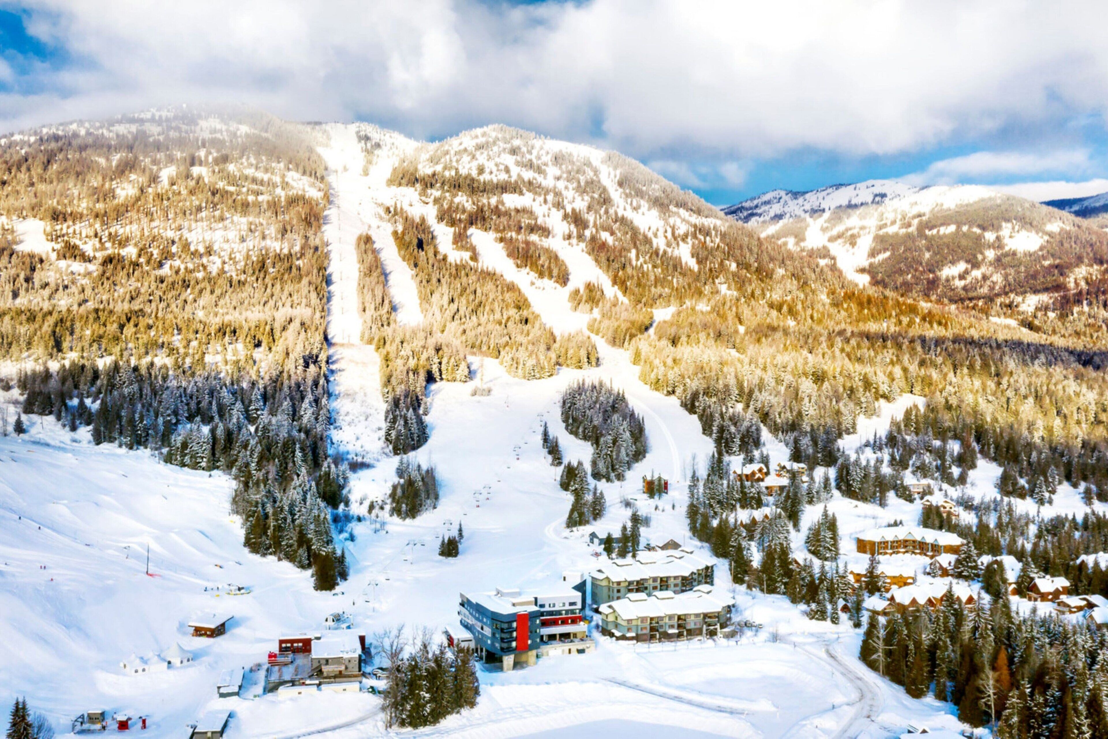 Une station de montagne enneigée, dotée de pistes de ski, de bâtiments d’hébergement et de zones boisées.