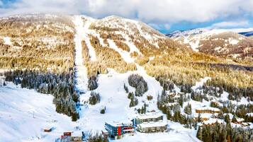 Une station de montagne enneigée, dotée de pistes de ski, de bâtiments d’hébergement et de zones boisées.