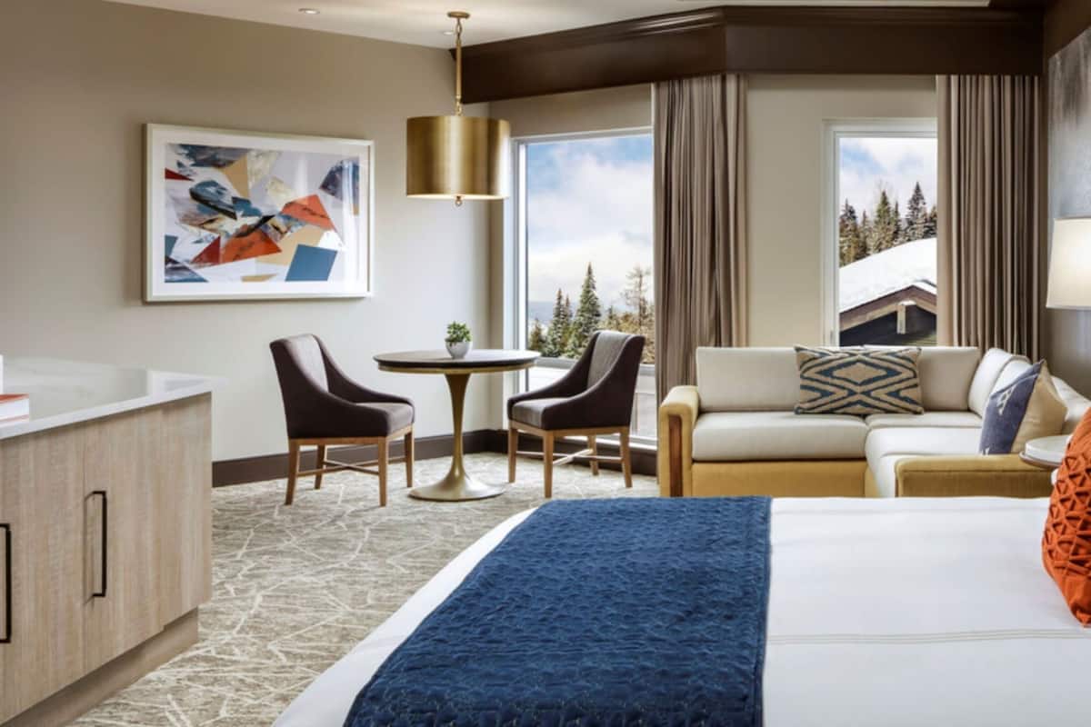 A hotel room with a large bed, a sofa, two armchairs, a small table, and a painting on the wall.