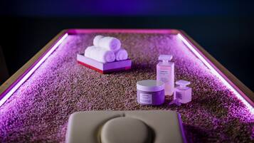 A table with a purple light, a stack of white towels, and two bottles of lotion.