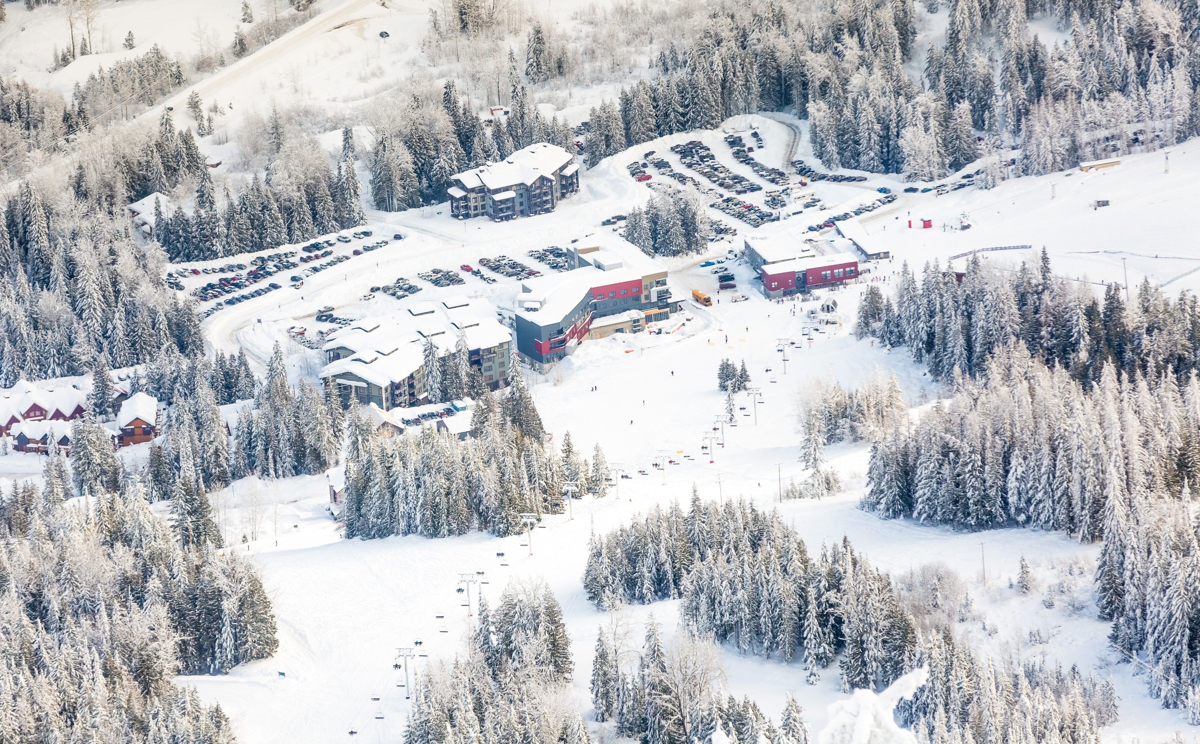 A snow-covered ski resort with multiple buildings, parking areas, and ski lifts.