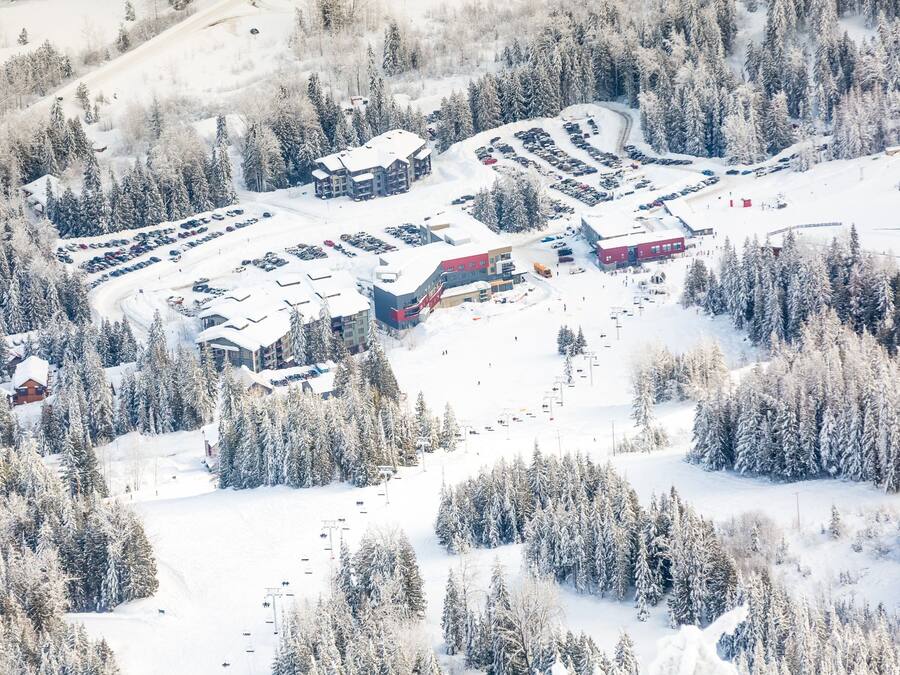 A snow-covered ski resort with multiple buildings, parking areas, and ski lifts.