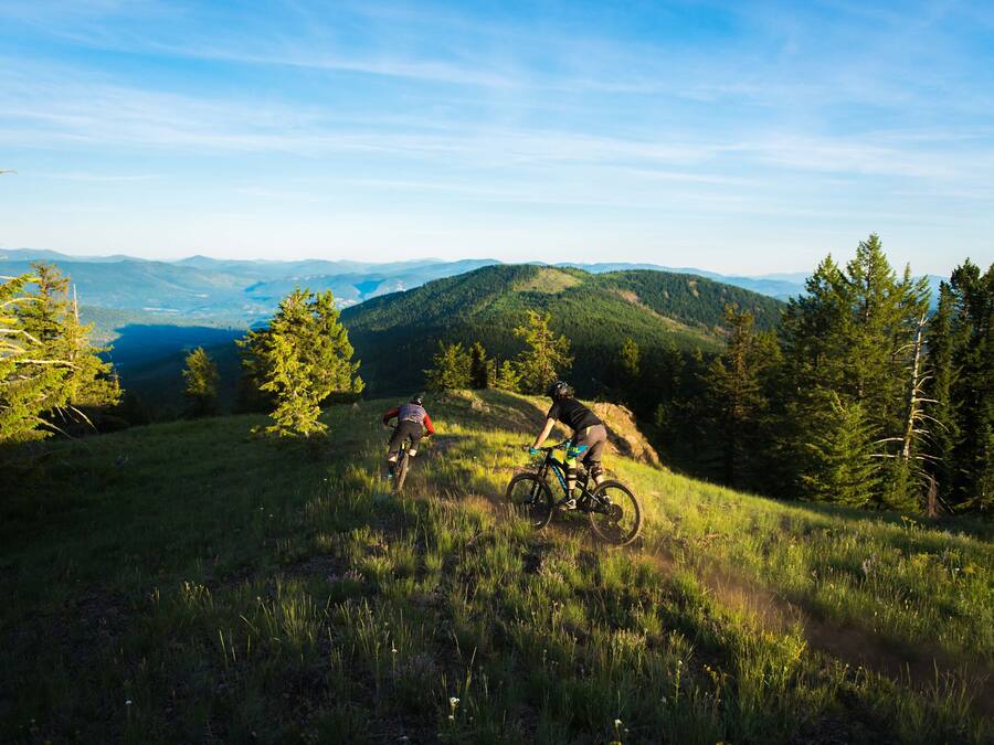 Deux vététistes sur un sentier, avec une vue sur des montagnes lointaines et un ciel dégagé.