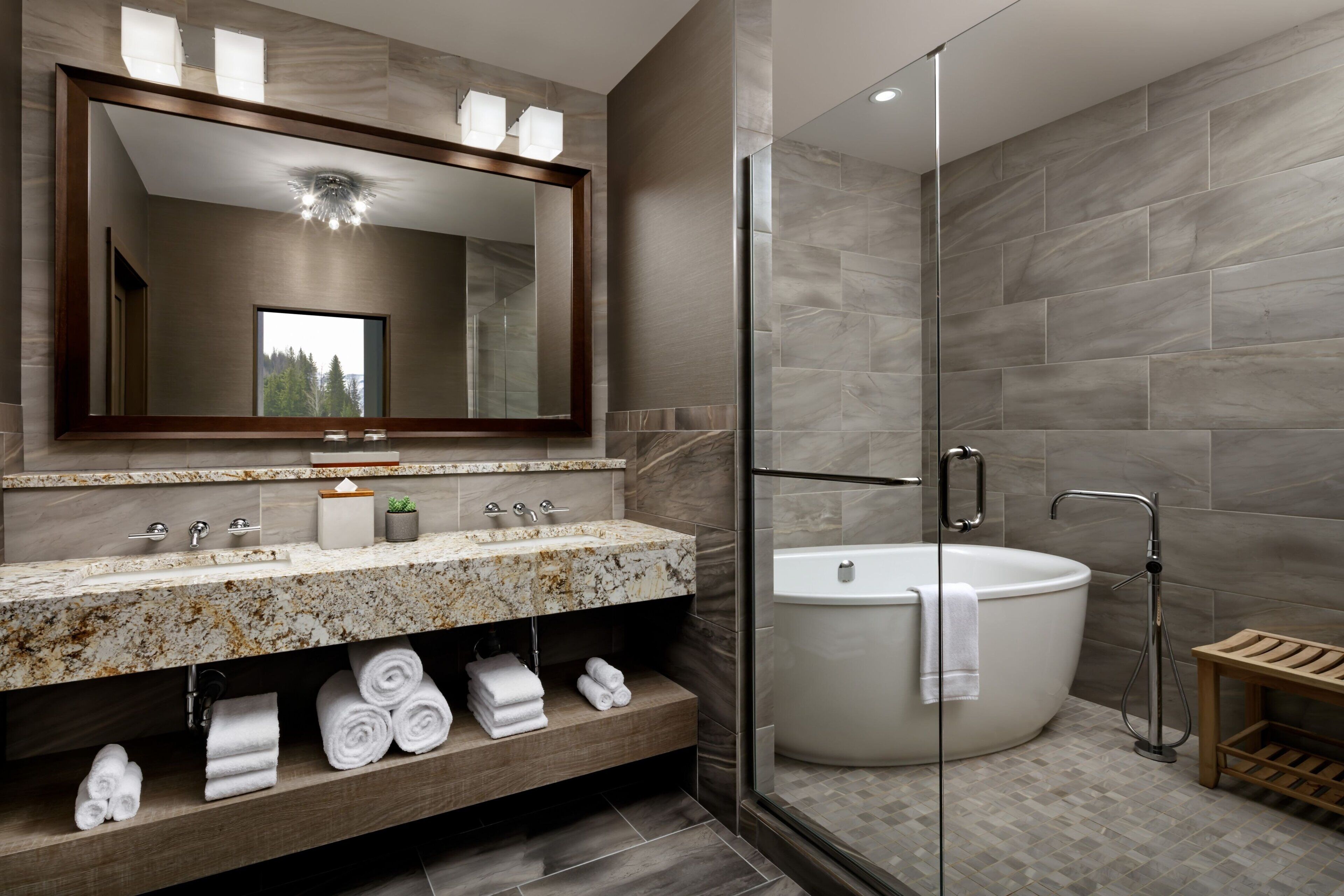 A modern bathroom with a large mirror, a marble sink, a bathtub, and a glass-enclosed shower.