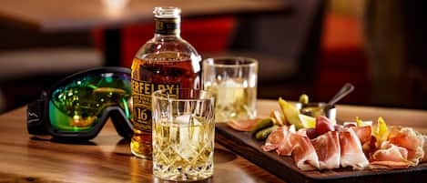 A bottle of whisky, two glasses, and a platter of meats on a wooden table.