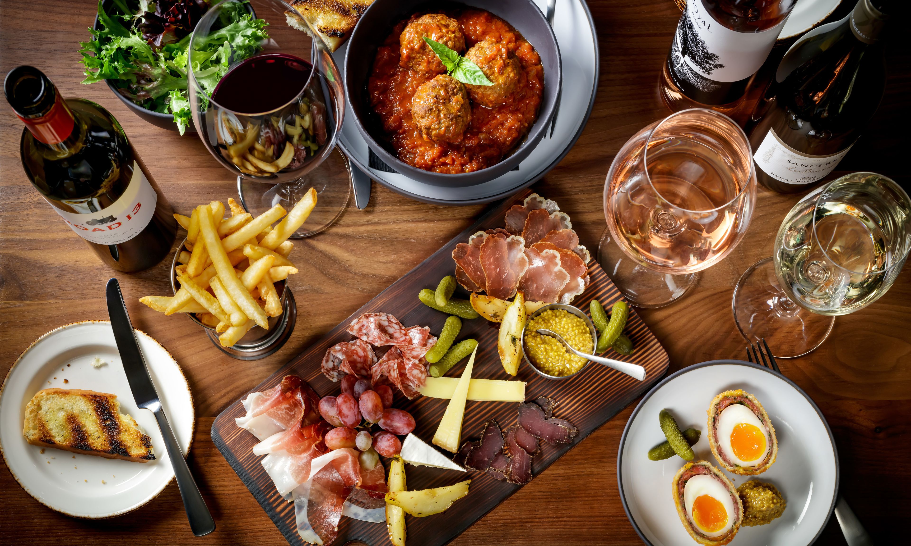 A table set with various food items, including meat, cheese, and bread, along with wine glasses and bottles.