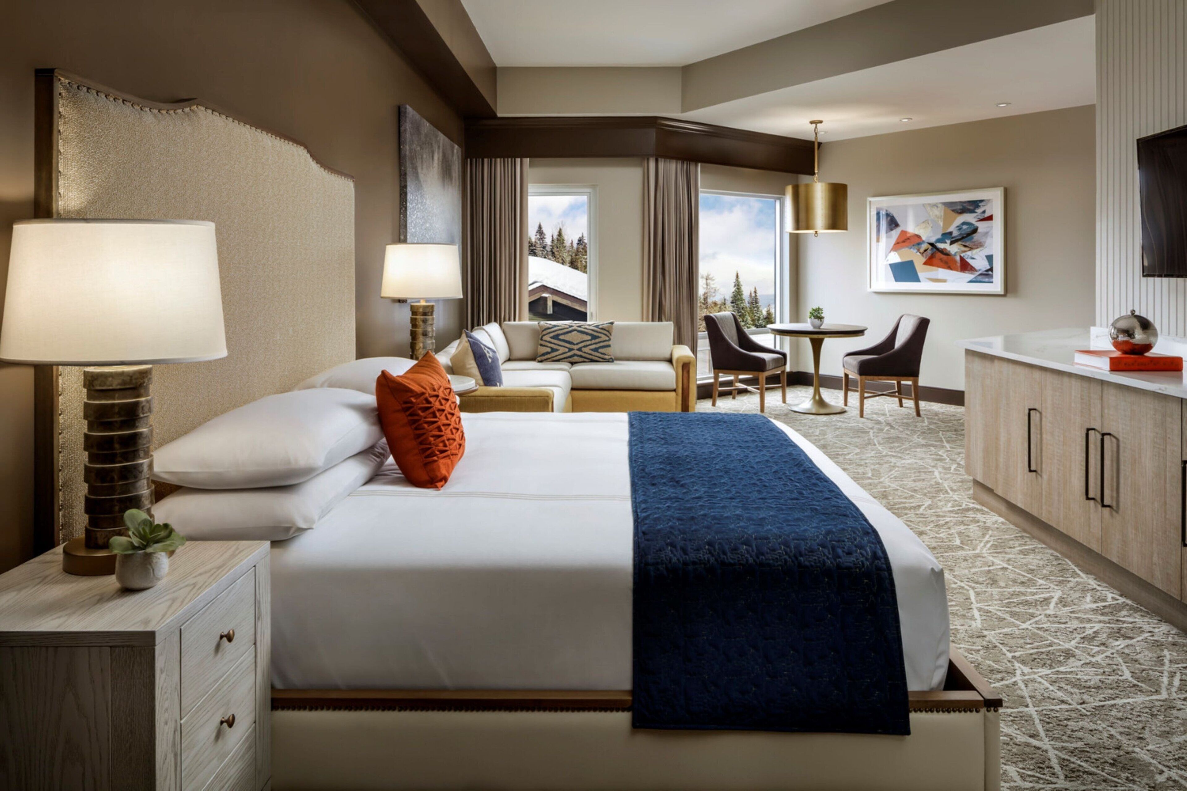A hotel room with a large bed, a desk, a chair, and a view of the outdoors.