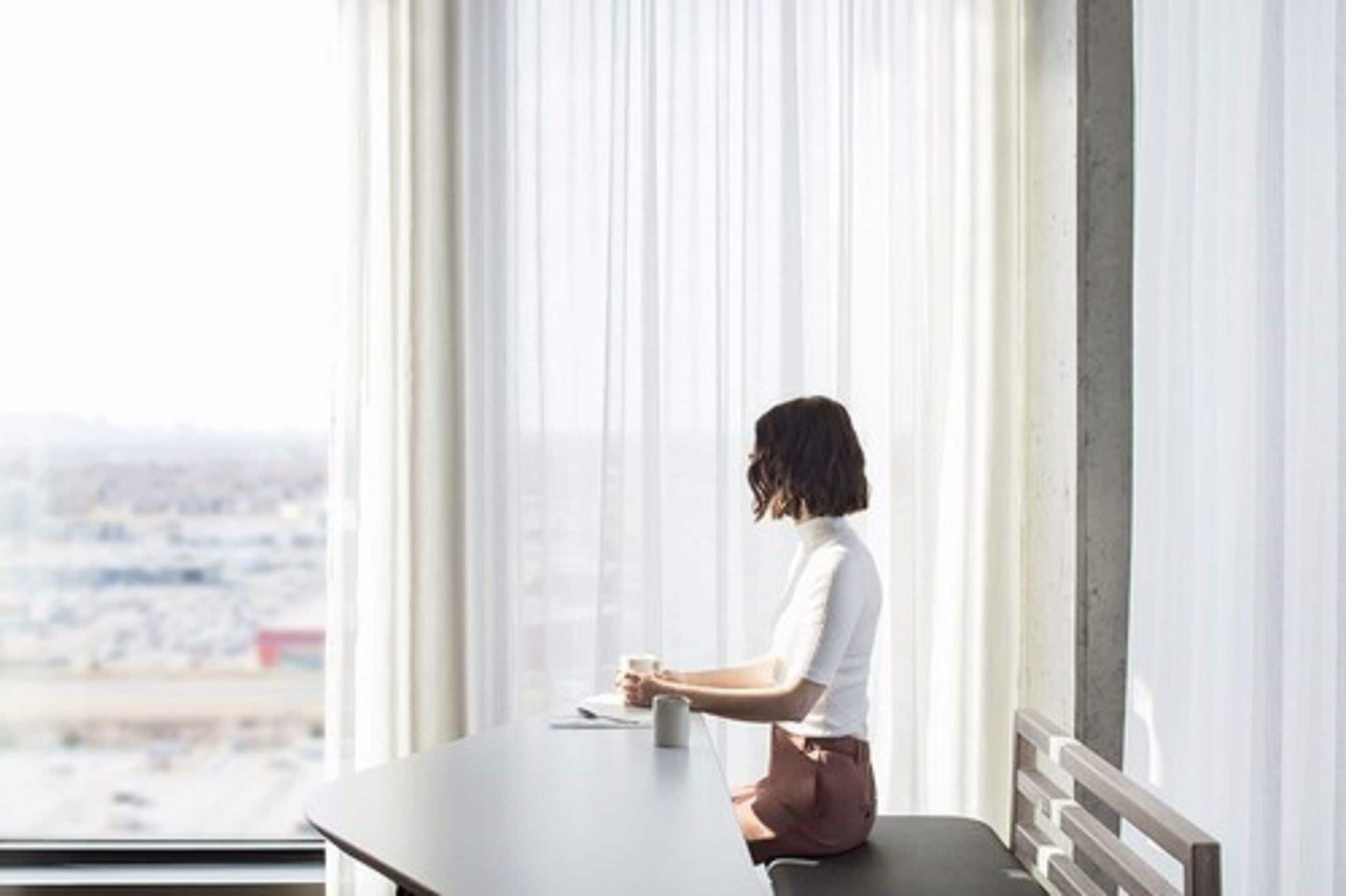 Eine Person sitzt an einem Tisch neben einem großen Fenster mit Blick auf die Stadt.