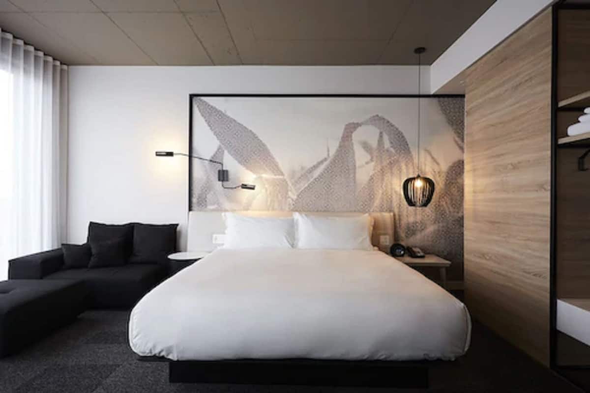 Ein modernes Hotelzimmer mit einem großen Bett, einer Couch, einem Nachttisch und einer Wandleuchte.