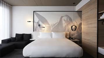 Una habitación de hotel moderna con una cama grande, un sofá, una mesita de noche y una lámpara de pared.