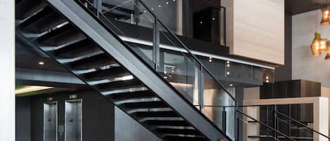 A modern lobby with a central seating area, a staircase, and a luggage trolley.