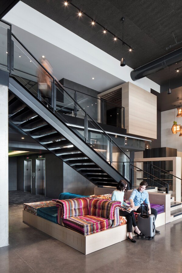 A modern lobby with a central seating area, a staircase, and a luggage trolley.