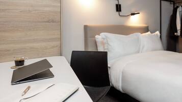 Habitación de hotel con una cama, un escritorio con una computadora portátil, una taza de café y un cuaderno.