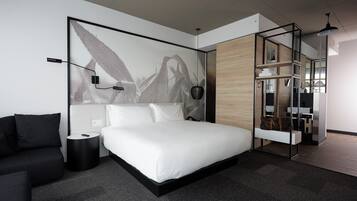A modern bedroom with a large bed, a small sofa, and a desk area.