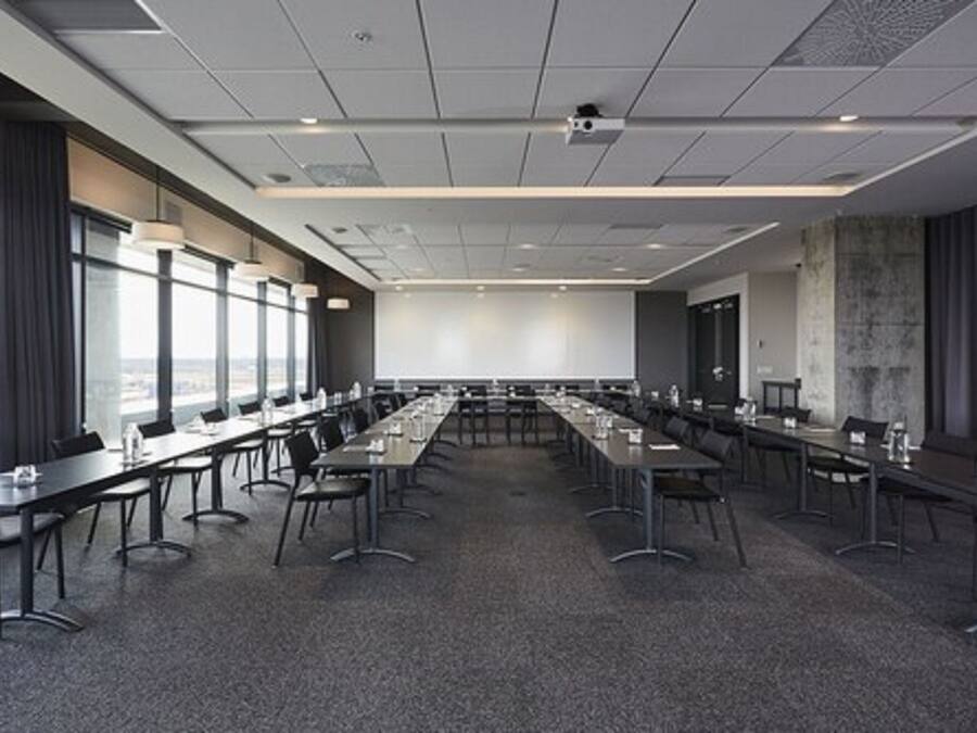 Un salón de conferencias con largas mesas, sillas y una pantalla grande al frente.