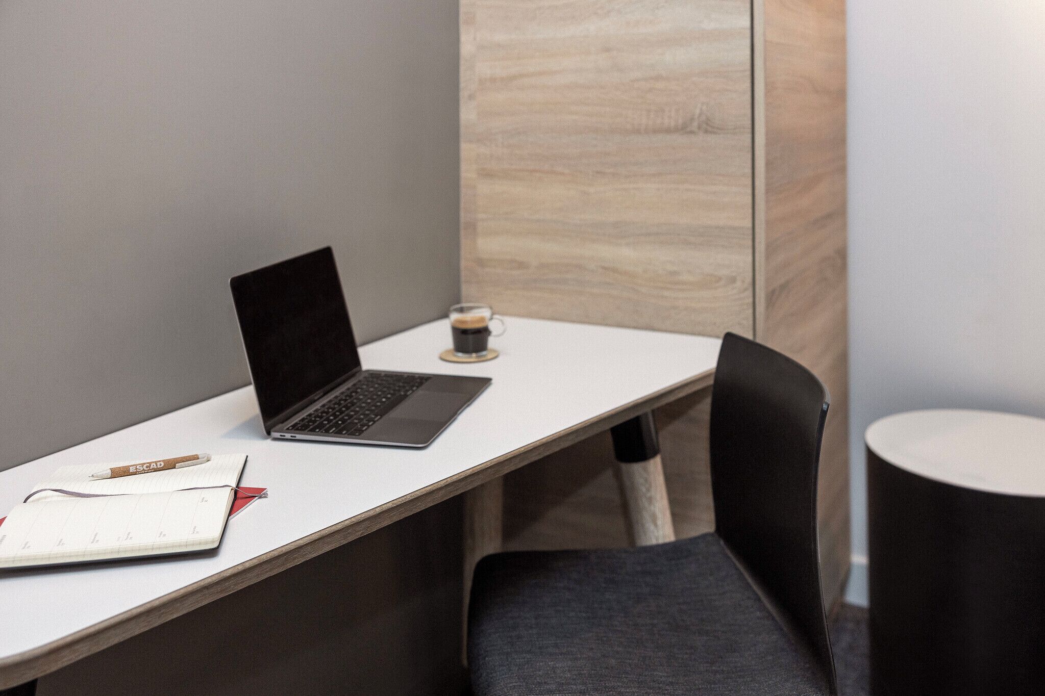 Un espace de travail avec un ordinateur portable, un carnet, un stylo et une tasse de café sur un bureau blanc.