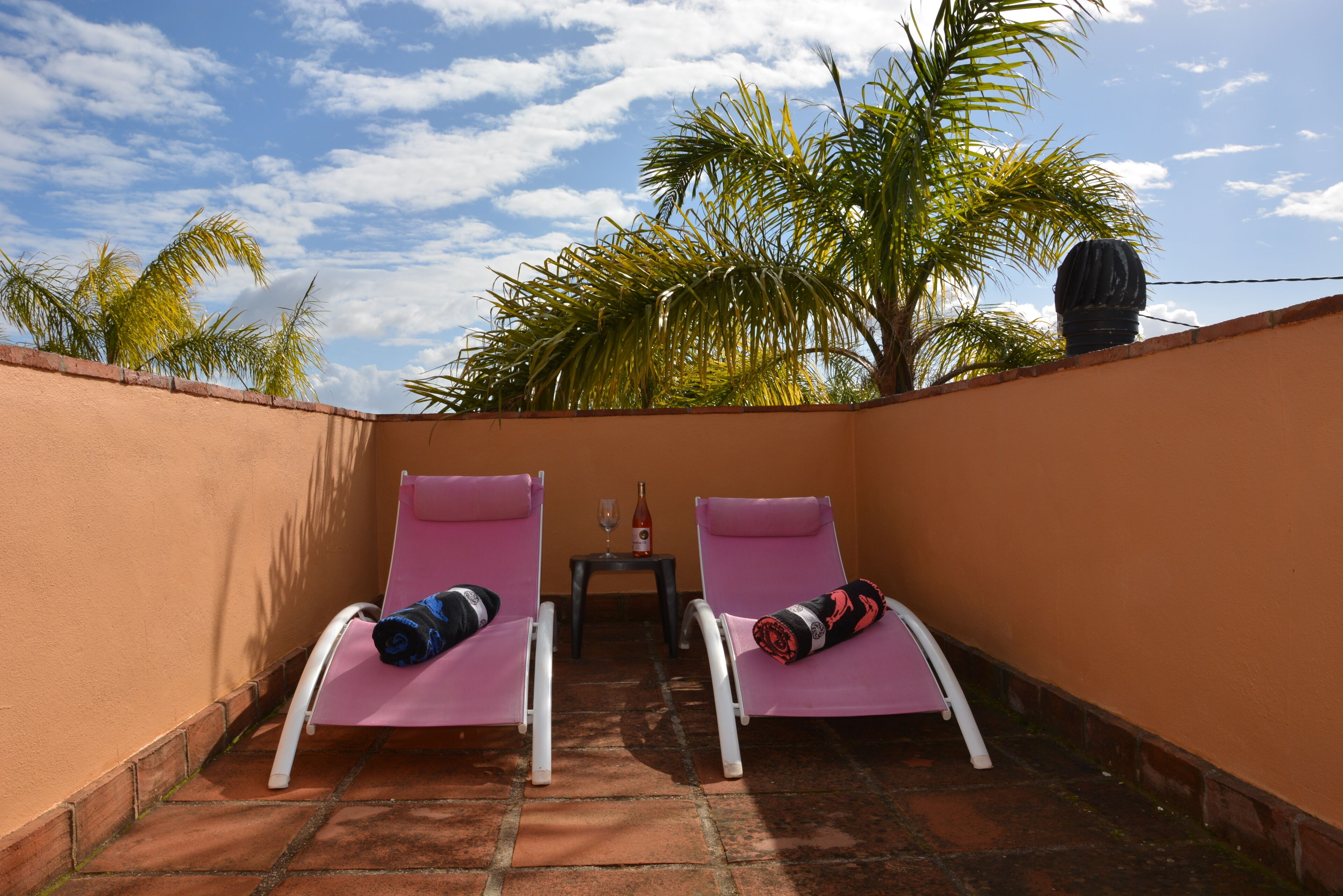 Un piccolo patio con due poltrone rosa, un tavolo con una bottiglia e un bicchiere, e una palma sullo sfondo.