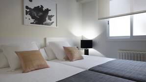 A hotel room with a large bed, a bedside table with a lamp, a window with blinds, and a wall-mounted artwork. - Playa de Ondarreta 2 by FeelFree Rentals (San Sebastián)