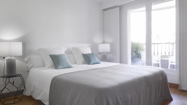 A modern hotel room with a large bed, two bedside lamps, and a view of the outdoors through a sliding glass door. - Playa de Ondarreta 2 by FeelFree Rentals (San Sebastián)