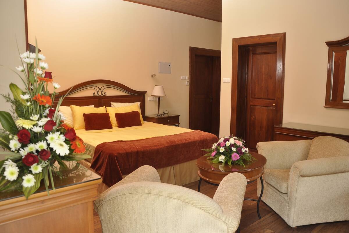 A hotel room with a bed, bedside table, lamp, chair, and a small table with flowers.