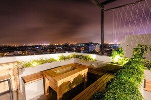 A rooftop terrace with wooden furniture, planters, and a view of the city at night. - Hanami Hotel Danang (Da Nang)