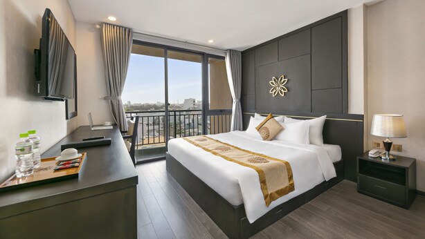 A hotel room with a bed, a desk with a laptop, a TV, and a view of the city. - Hanami Hotel Danang (Da Nang)
