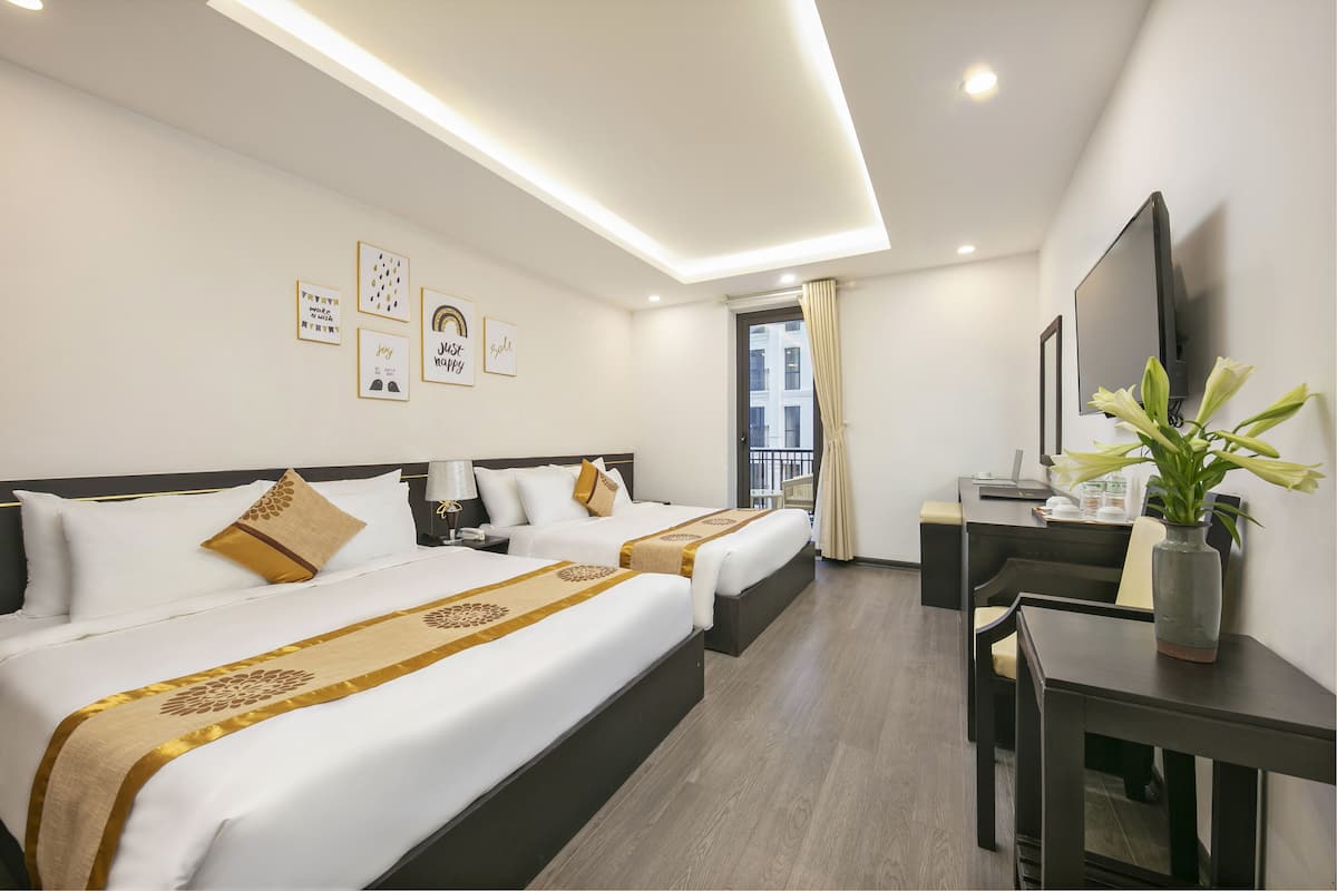 A hotel room with two beds, a desk, a chair, a TV, and artwork on the walls.