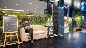 A man sitting on a sofa in a hotel lobby with a chalkboard sign advertising rent, a small table with books, and a statue. - Hanami Hotel Danang (Da Nang)