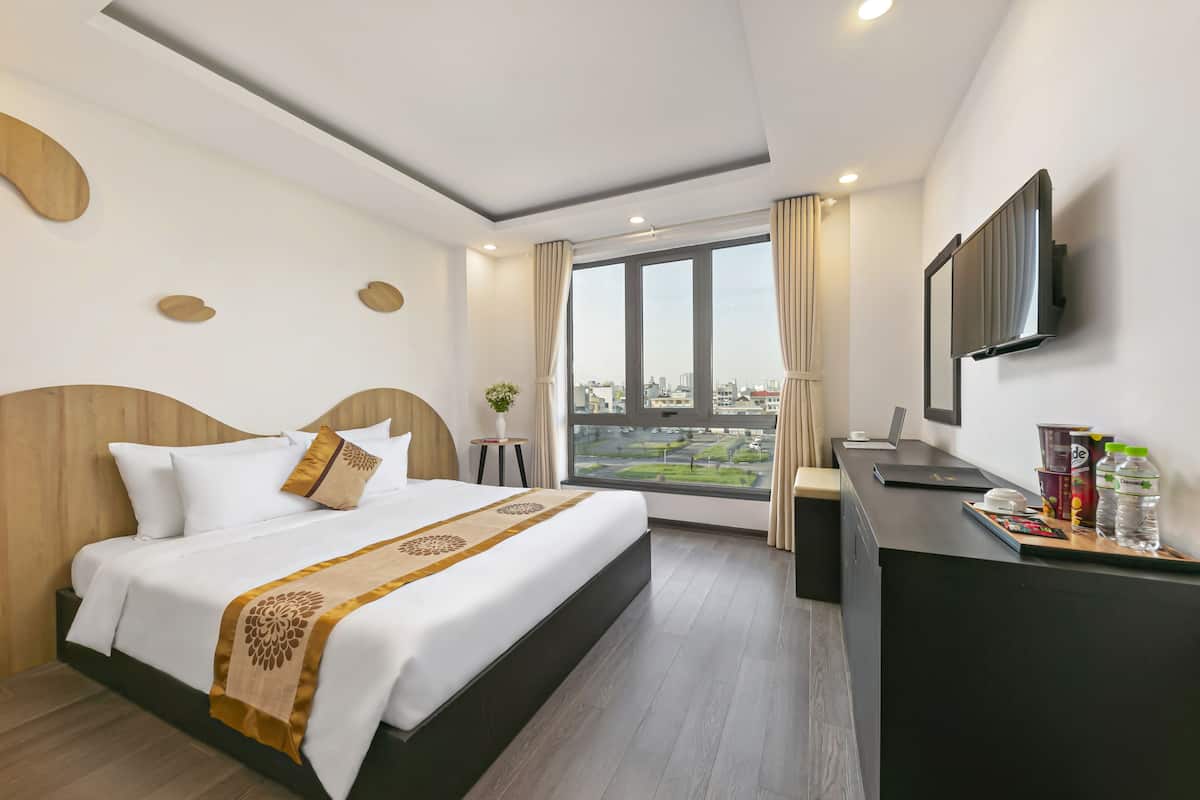 A hotel room with a large bed, a desk with a computer, and a view of the city through the window.