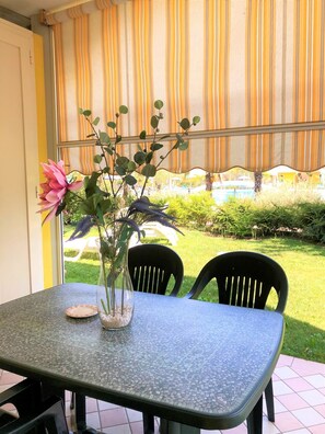 Une table de patio avec des chaises, un vase rempli de fleurs et une vue sur une piscine et la verdure environnante.