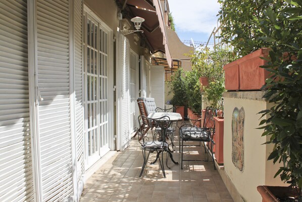 Une terrasse couverte avec une table et des chaises, une plante en pot et un luminaire fixé au mur.