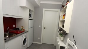 A compact kitchen with a washing machine, a microwave, and a red drying rack.