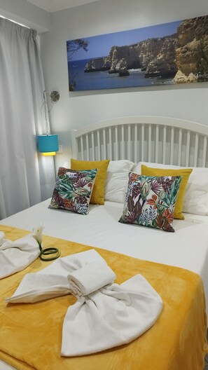Una camera d'albergo con un letto, cuscini, un comodino, una lampada e un quadro raffigurante una costa.