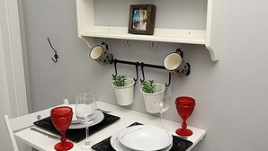 Uma sala de jantar com uma mesa e cadeiras brancas, uma estante com pratos decorativos e um suporte na parede para xícaras.