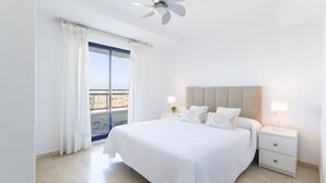 Ein Hotelzimmer mit einem großen Bett, einem Deckenventilator, einem Nachttisch mit Lampe und Blick auf die Stadt durch das Fenster.