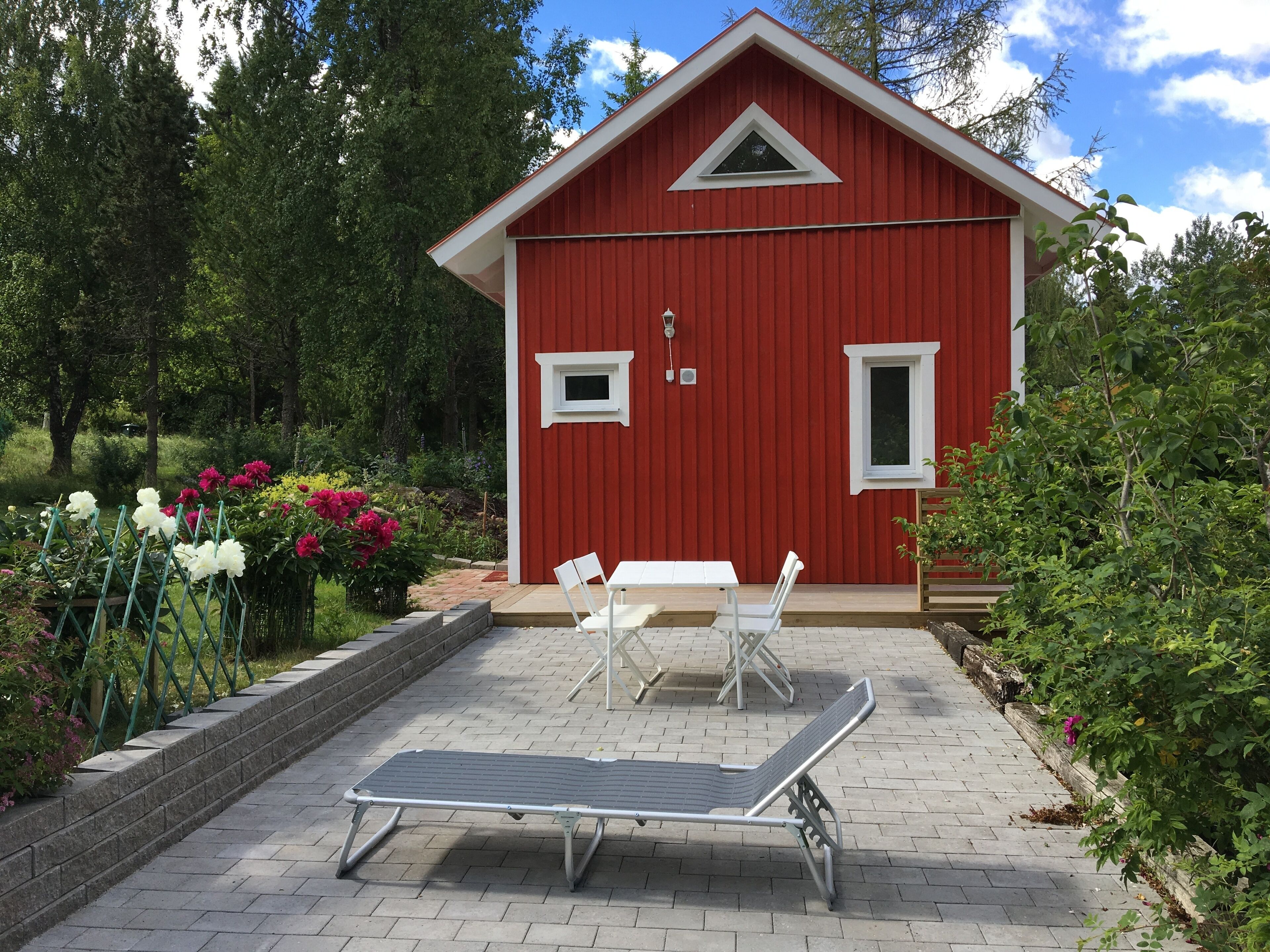 A red building with a small porch, white chairs, and a metal sun lounger.