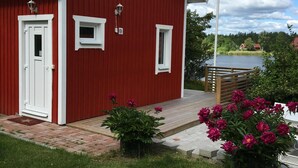 Ein rotes Gebäude mit weißer Tür und Fenstern, einer Fahnenstange und einem Garten mit rosa Blumen.