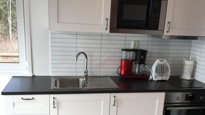 Eine moderne Küche mit weißen Schränken, einer schwarzen Arbeitsplatte, einer Edelstahl-Spüle, einer Mikrowelle, einer Kaffeemaschine und einem Backofen.