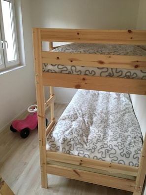 Una cama litera con colchón estampado, estructura de madera y un coche de juguete rosa en la habitación.