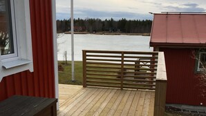 Eine Holzterrasse mit Blick auf einen See, ein rotes Gebäude und ein weißes Fenster.