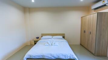A neatly made bed with white linens and two swan-shaped towels, a wooden wardrobe, and a small bedside table with a lamp.