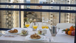 Una mesa de desayuno con cruasanes, jugo de naranja y un bol de fruta, con vistas a la ciudad.