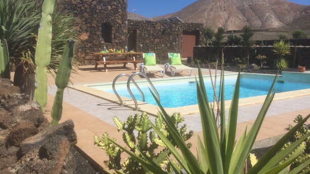 A pool area with a stone wall, a table with chairs, and a mountain in the background. - ECO Friendly Volcanic Rock Villa with Private Pool (6.7m x 4.6m) WiFi. Sea View. (Villa Verde)